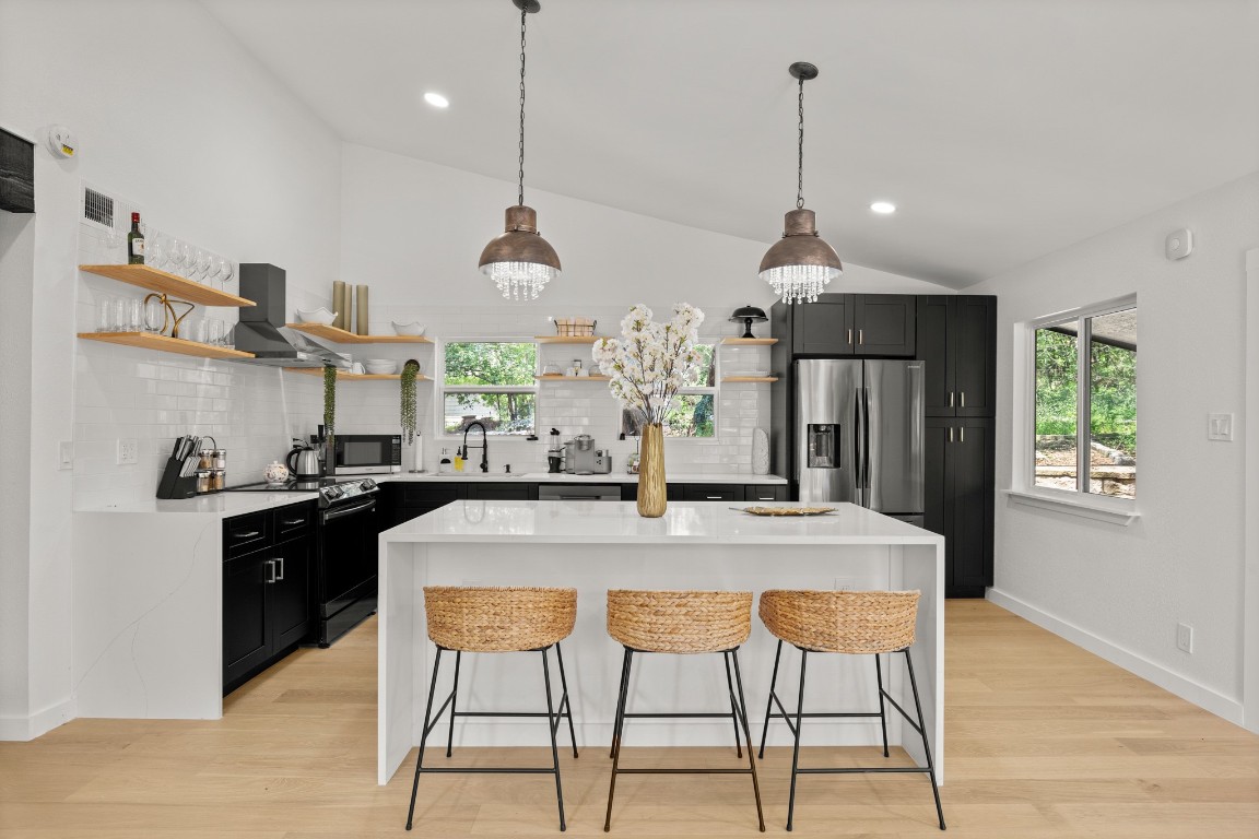 3904 Highland Drive Austin, TX 78734 - Photo 9 of 37 Kitchen with dark cabinets, a breakfast bar area, a center island, pendant lighting, and light stone counters