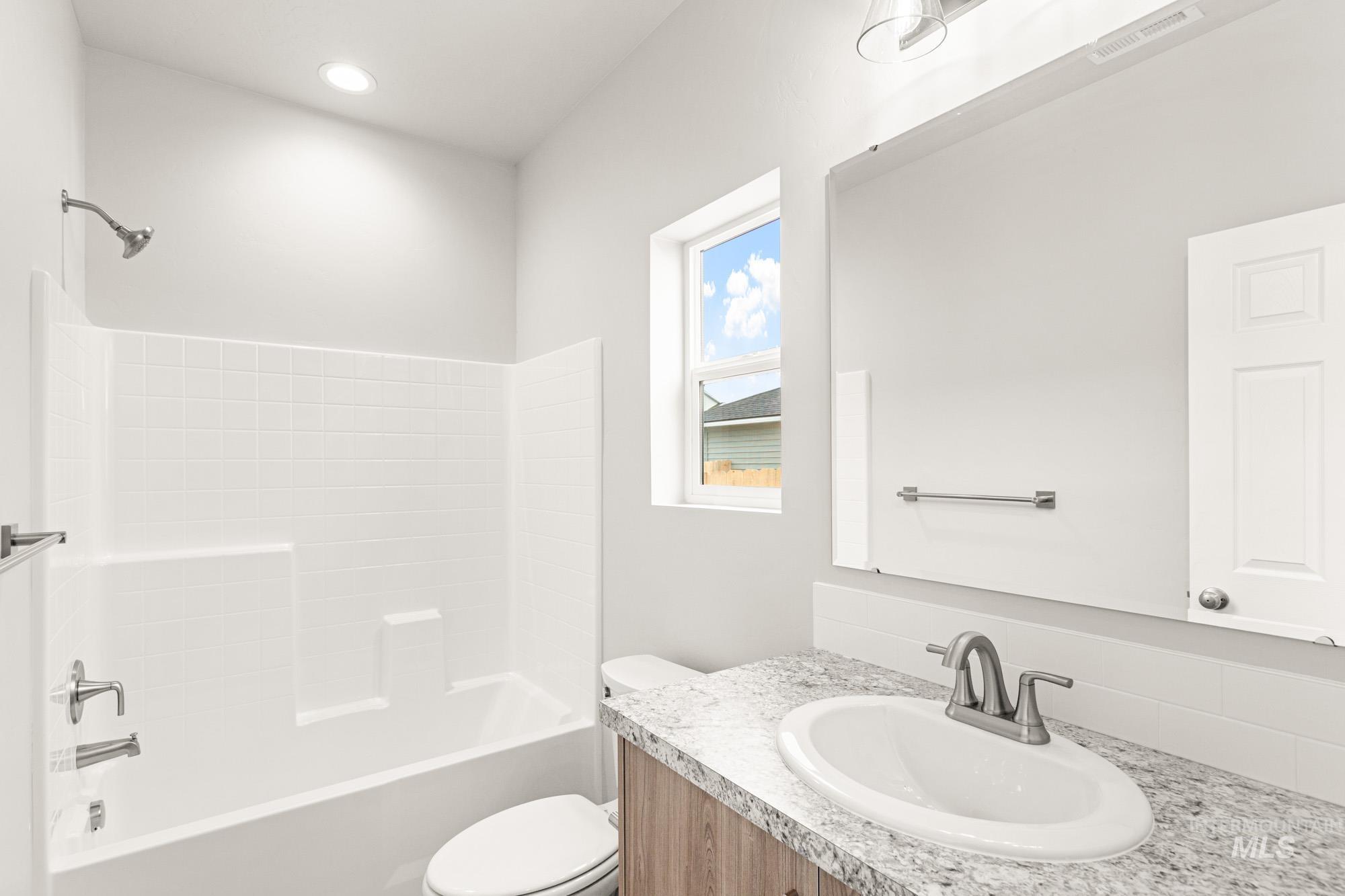 448 Merlin Court Middleton, ID 83644 - Photo 15 of 29 Built-in bathtub with white tile surround, vanity with granite-style countertop, integrated sink, and wood-finish cabinetry
