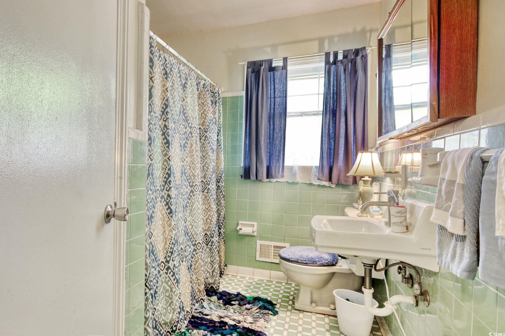 2004 Seitter Street Georgetown, SC 29440 - Photo 20 of 33 Bathroom featuring toilet, curtained shower, tile walls, tile patterned flooring, and wainscoting