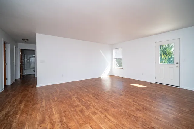 a view of an empty room with wooden floor and a window