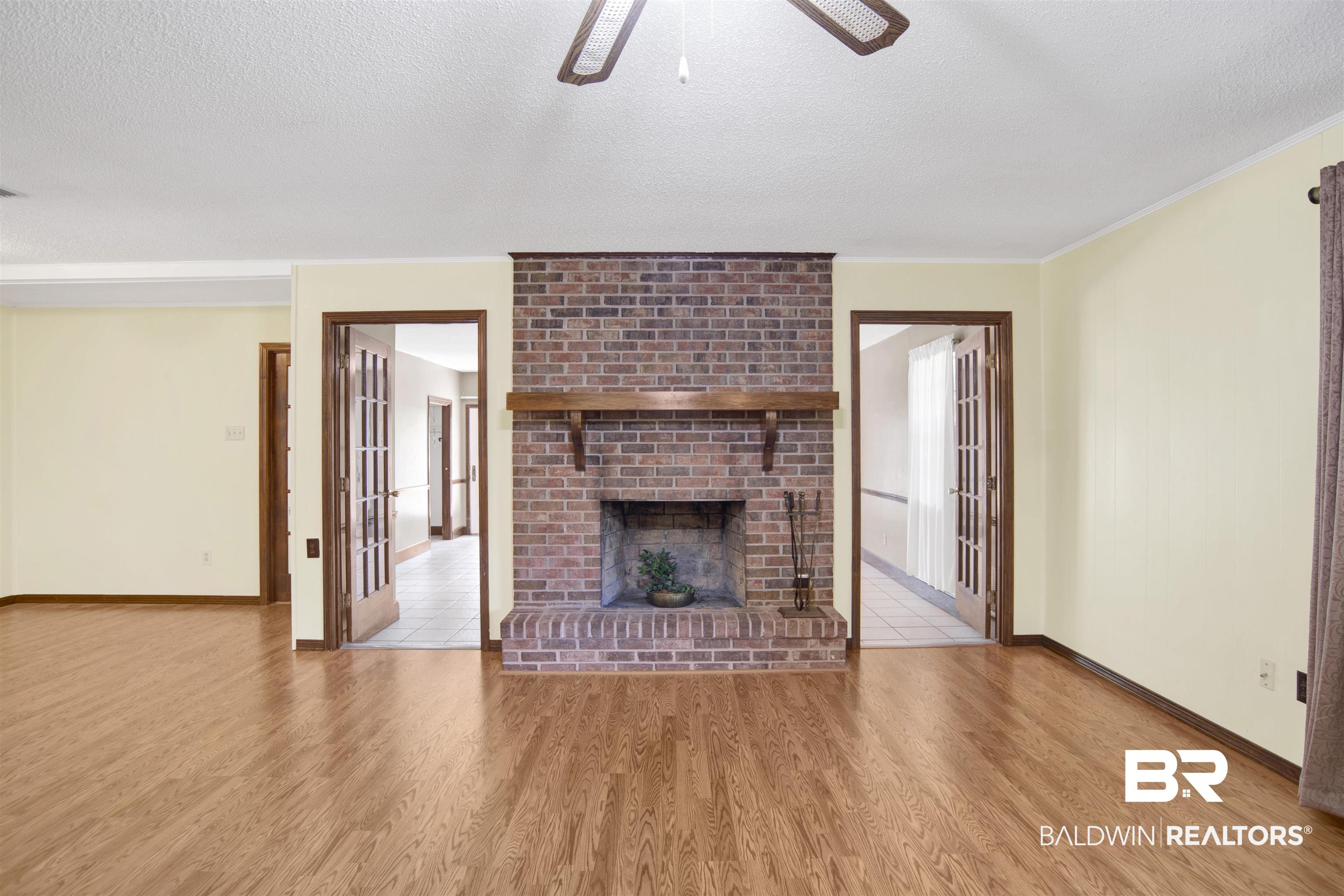 30888 Cemetery Road Daphne, AL 36527 - Photo 3 of 36 Brick fireplace with a wood mantel, wood-finish flooring, light-colored walls, and two sets of glass-paneled French doors