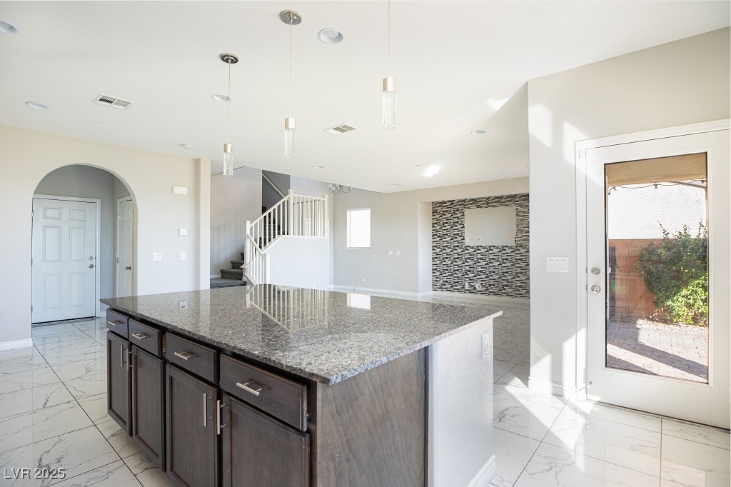 6856 Pivot Point Street Las Vegas, NV 89148 - Photo 17 of 32 Kitchen featuring arched walkways, dark stone countertops, pendant lighting, a kitchen island, and light marble finish flooring