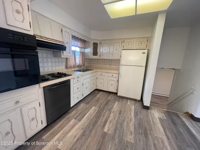 a kitchen with granite countertop white cabinets a sink a stove a refrigerator and wooden floors