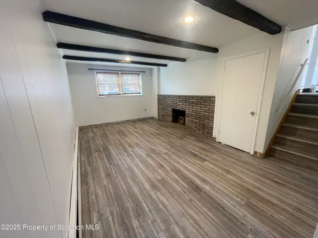 a view of an empty room with wooden floor fireplace and a window