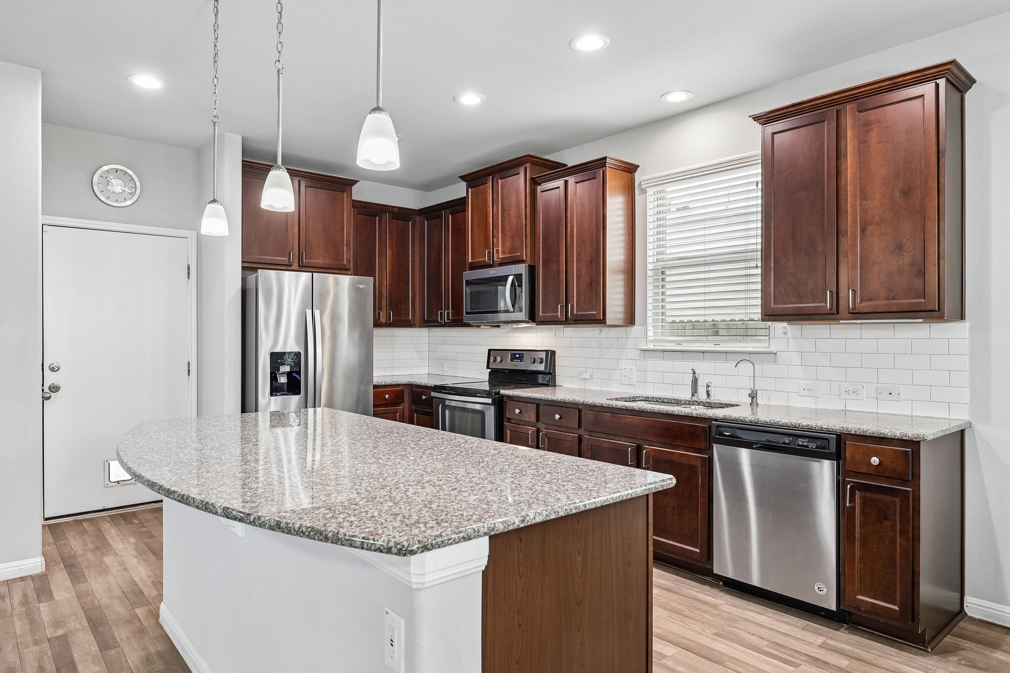 387 Guemal Road Buda, TX 78610 - Photo 14 of 39 Kitchen featuring a substantial island with a speckled countertop, rich wood-finish cabinetry, stainless steel appliances, a subway tile backsplash, and wood-finish flooring