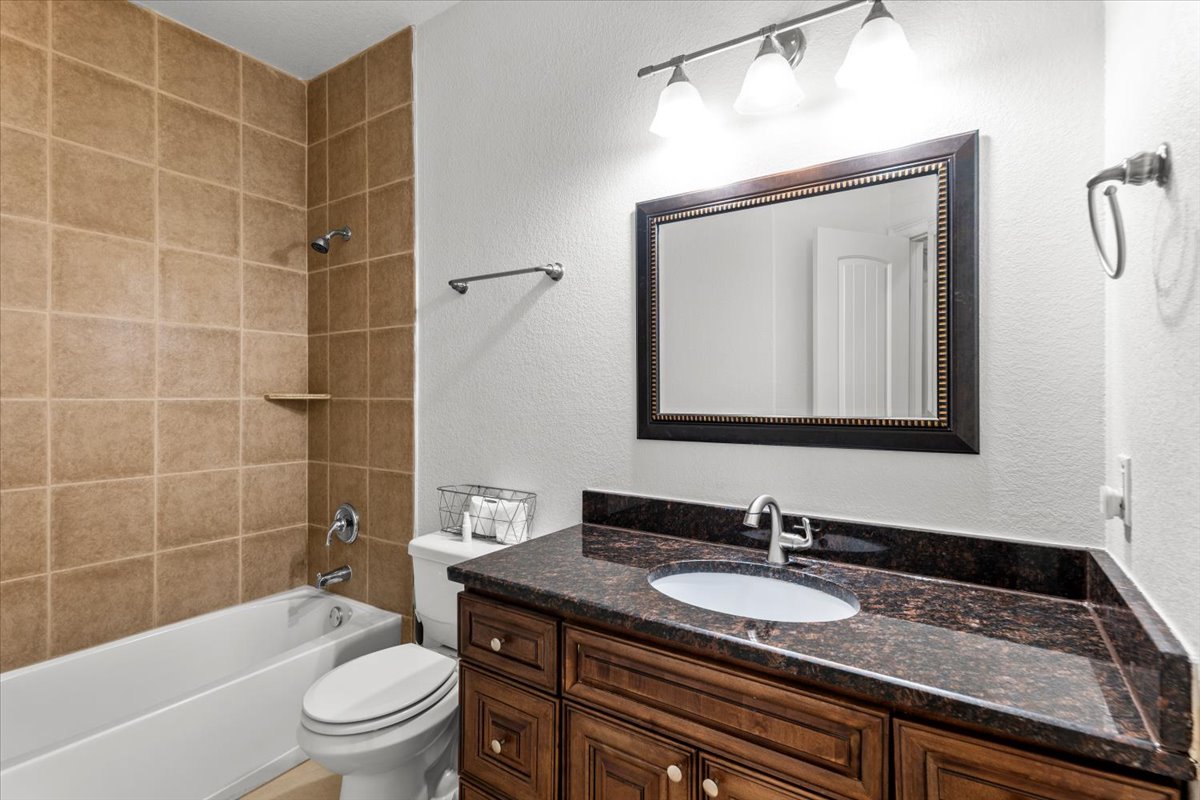 437 Balch Road Elgin, TX 78621 - Photo 20 of 37 A dark granite vanity with ample storage complements the tiled tub and shower in this practical bathroom.