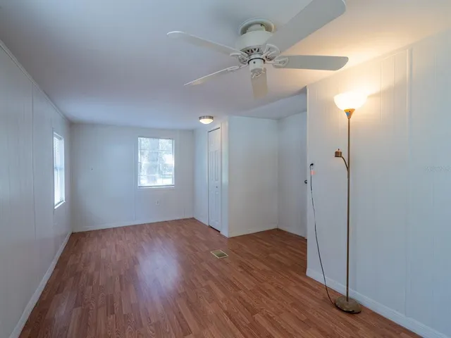 an empty room with wooden floor chandelier fan and windows