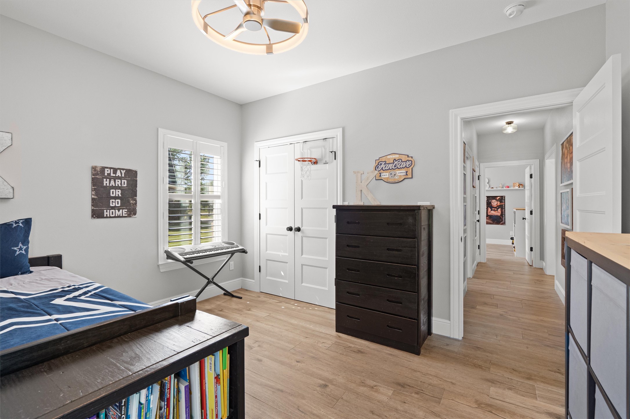 136 Fawn Hollow Elgin, TX 78621 - Photo 28 of 40 Bedroom 3 featuring light wood-finish flooring, a contemporary ceiling fan with integrated lighting, a window with white plantation shutters, and a double-door closet with black hardware