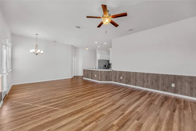 a view of an empty room with wooden floor and a ceiling fan