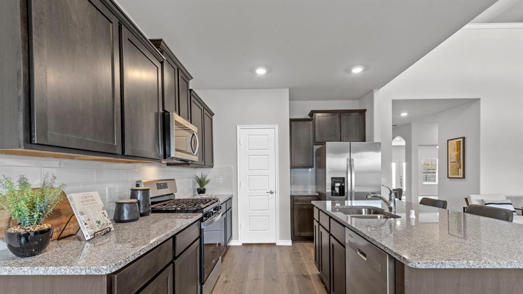 500 Range Road Caddo Mills, TX 75135 - Photo 31 of 35 Kitchen featuring dark wood-finish cabinetry, light granite countertops, stainless steel appliances, a white subway tile backsplash, and wood-finish flooring