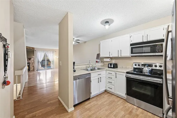 a kitchen with stainless steel appliances granite countertop a stove top oven a sink dishwasher and white cabinets with wooden floor