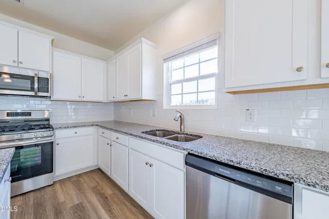 a kitchen with granite countertop stainless steel appliances white cabinets granite counter tops and a wooden floors