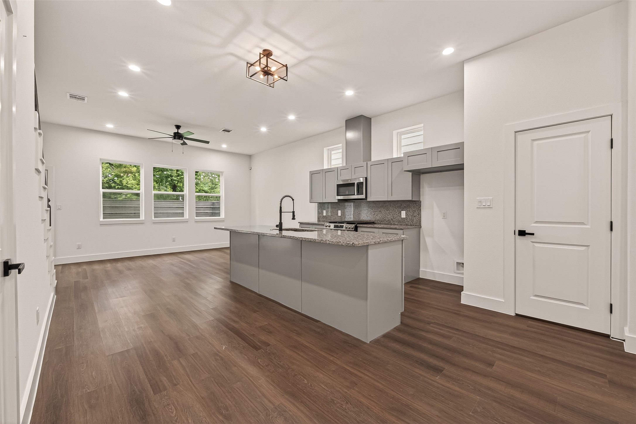 6808 Madrid Street Houston, TX 77021 - Photo 8 of 31 This photo showcases a modern, open-concept kitchen and living area with sleek engineer wood floors, neutral walls, and ample natural light from multiple windows. The kitchen features a large island with granite countertops, stainless steel appliances, and stylish gray cabinetry, perfect for entertaining and everyday living.