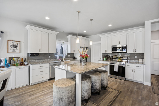 7889 Bristlecone Road Eagle Mountain, UT 84005 - Photo 11 of 42 Kitchen featuring white cabinetry, granite countertops, stainless steel appliances, a tile backsplash, and wood-finish flooring