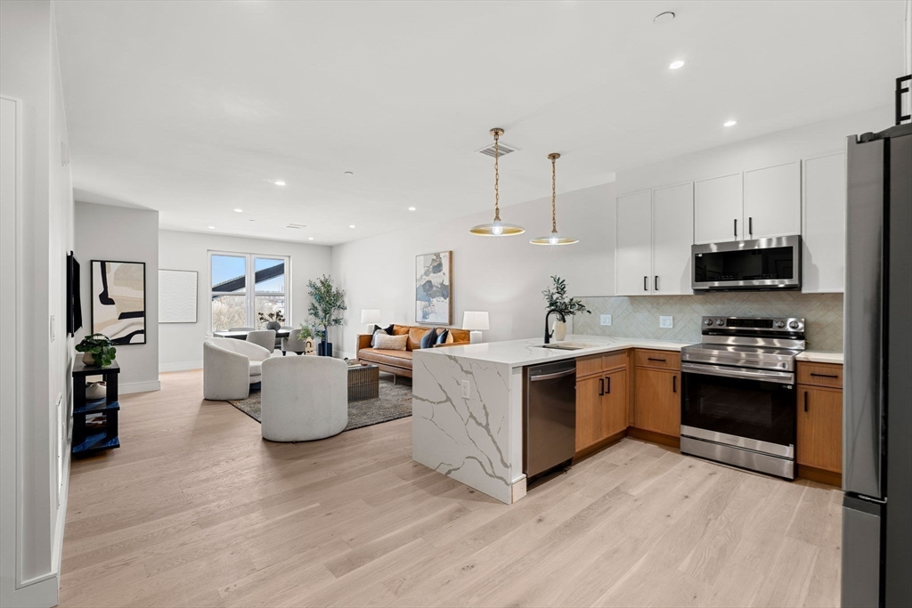 27 Guild Street, Unit 301 Boston, MA 02119 - Photo 6 of 29 a large kitchen with stainless steel appliances kitchen island granite countertop a stove top oven a sink dishwasher and white cabinets with wooden floor