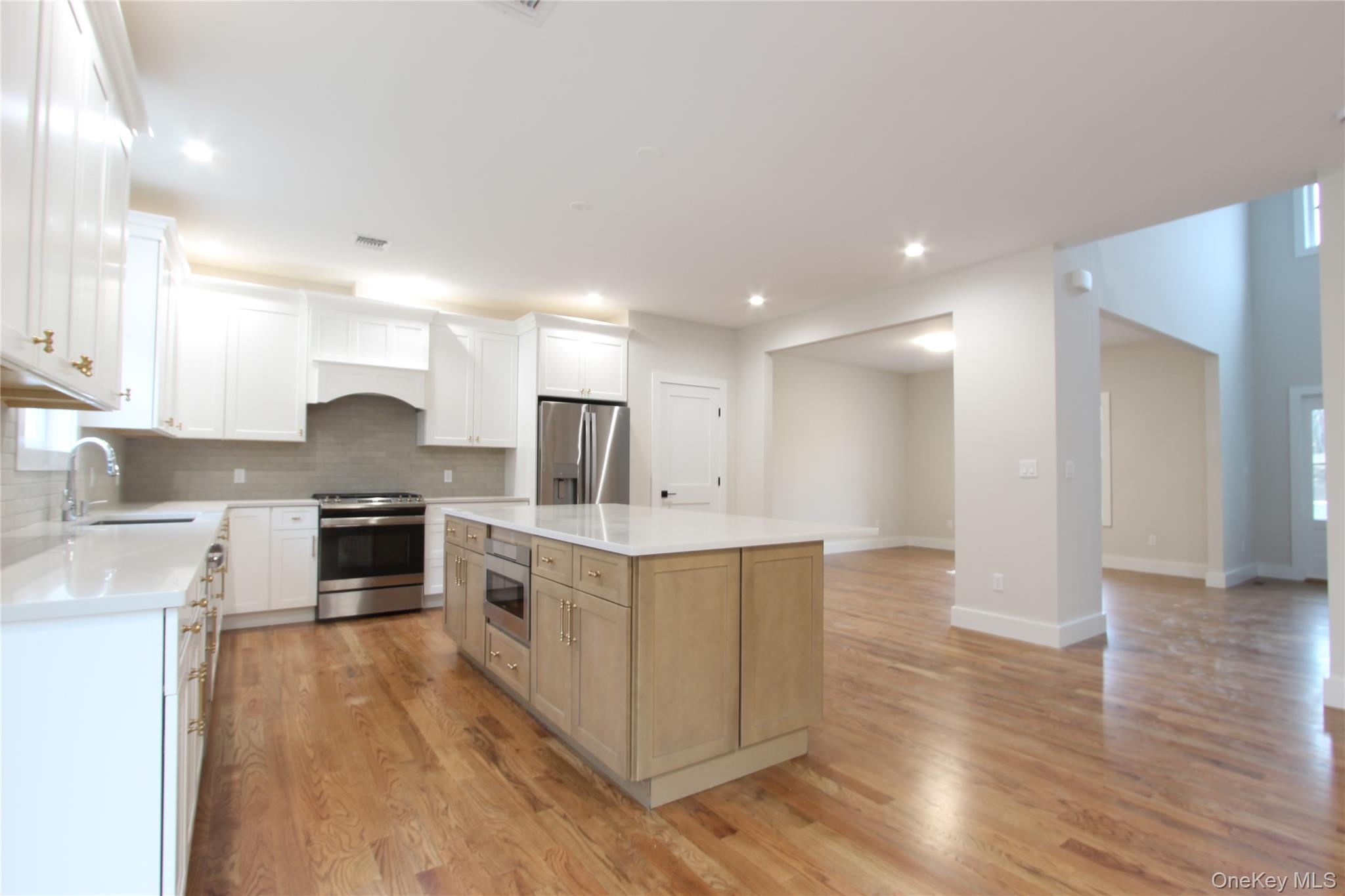 5 Colonels Path Manorville, NY 11949 - Photo 4 of 19 Kitchen featuring stainless steel appliances, light wood finished floors, backsplash, light countertops, and white cabinetry