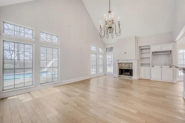 a view of an empty room with chandelier fireplace and wooden floor