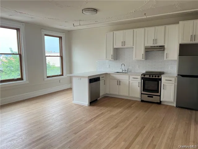 a kitchen with stainless steel appliances a stove a sink and white cabinets with wooden floor