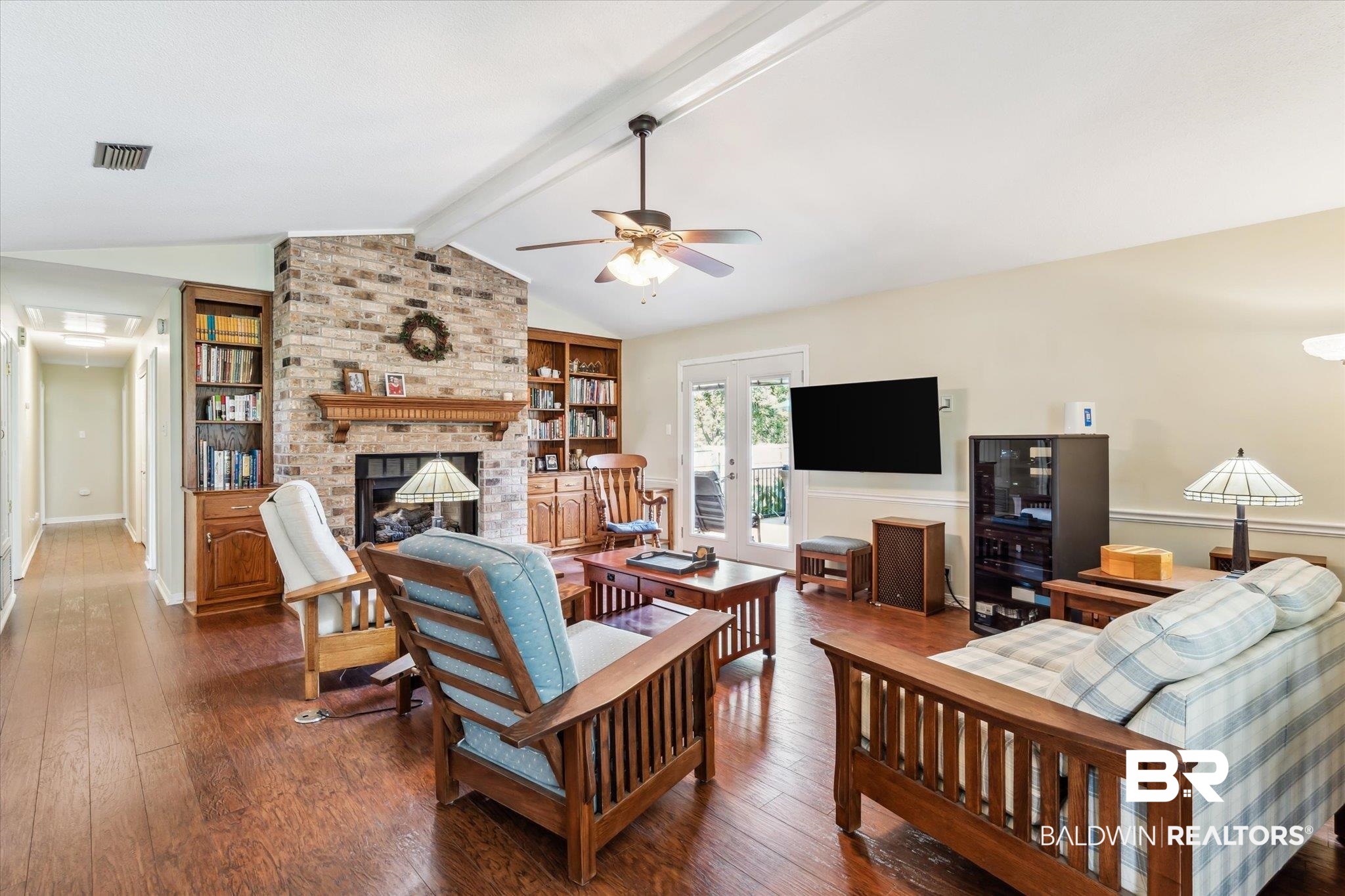 8710 Three Notch Road Mobile, AL 36619 - Photo 3 of 30 Living room featuring lofted ceiling with beams, ceiling fan, a brick fireplace, brick wall, and dark hardwood / wood-style flooring