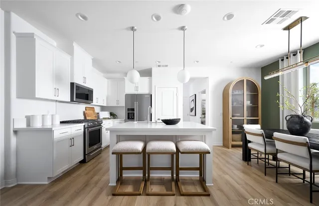 a kitchen with stainless steel appliances kitchen island granite countertop a stove a sink dishwasher a dining table and chairs with wooden floor