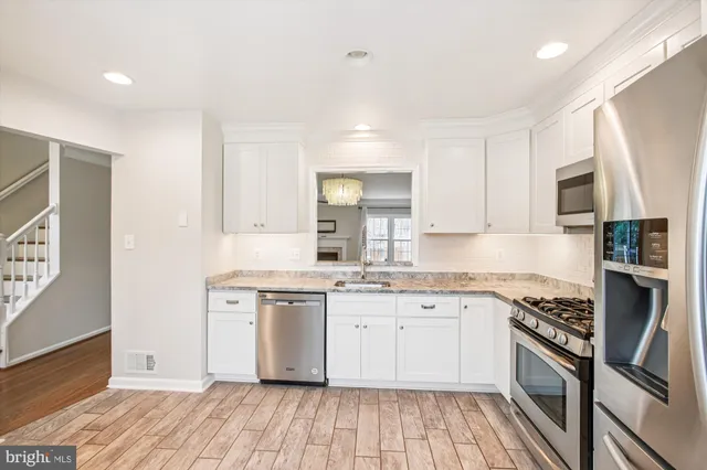 a kitchen with stainless steel appliances granite countertop a stove top oven a sink dishwasher and a refrigerator with wooden floor