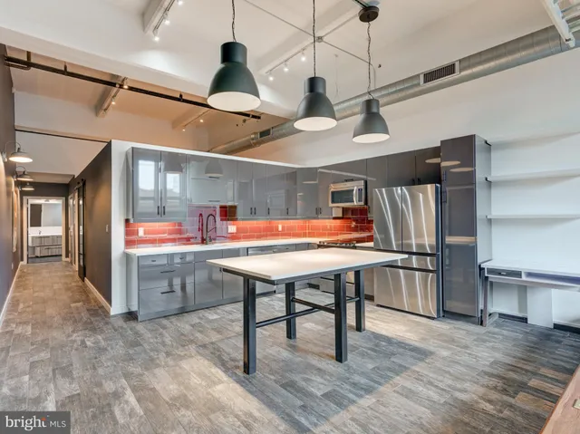 a room with lots of wooden furniture a rug potted plant and kitchen view