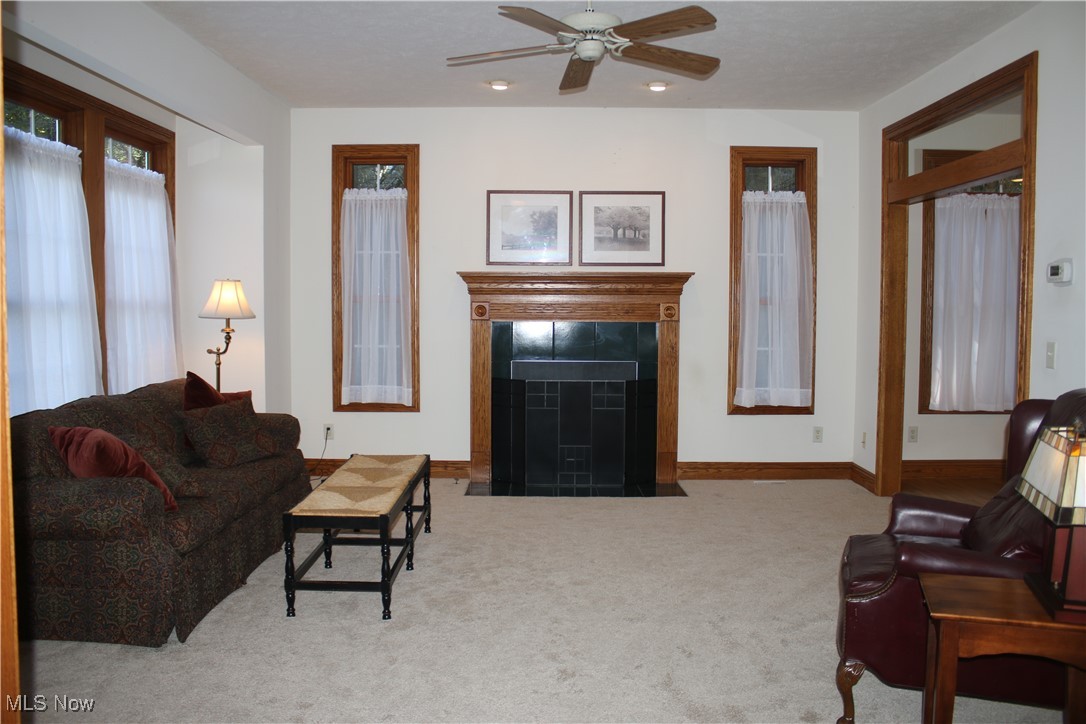 Carpeted living room featuring a tiled fireplace, ceiling fan, and recessed lighting