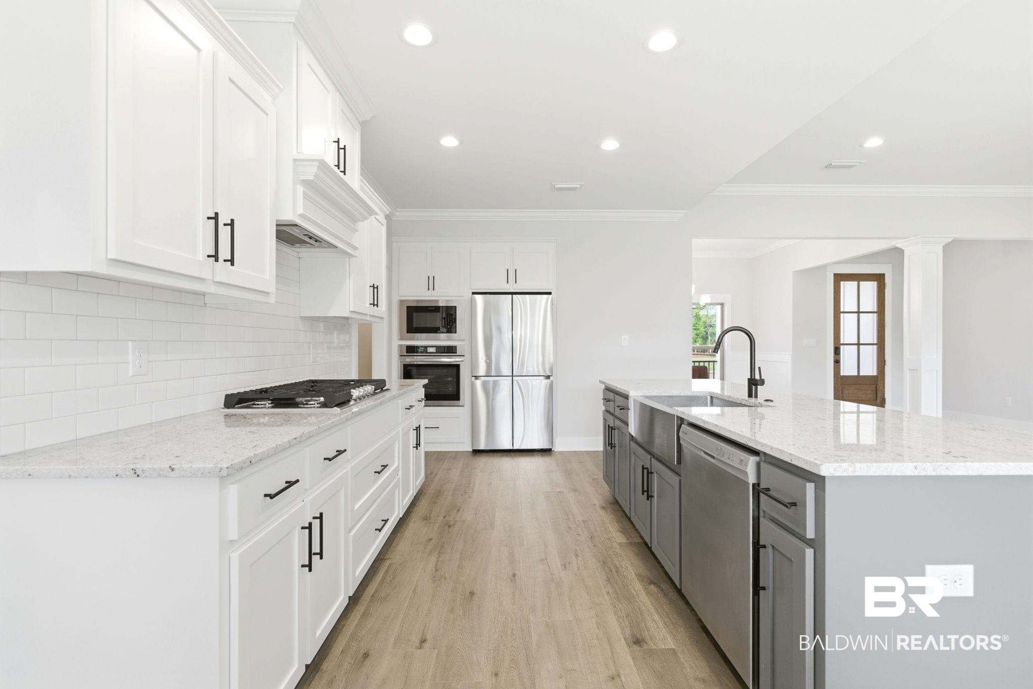 12132 Exbury Way Daphne, AL 36527 - Photo 11 of 47 Kitchen with two tone color scheme, a spacious island, stainless steel appliances, light stone countertops, and light wood-style flooring