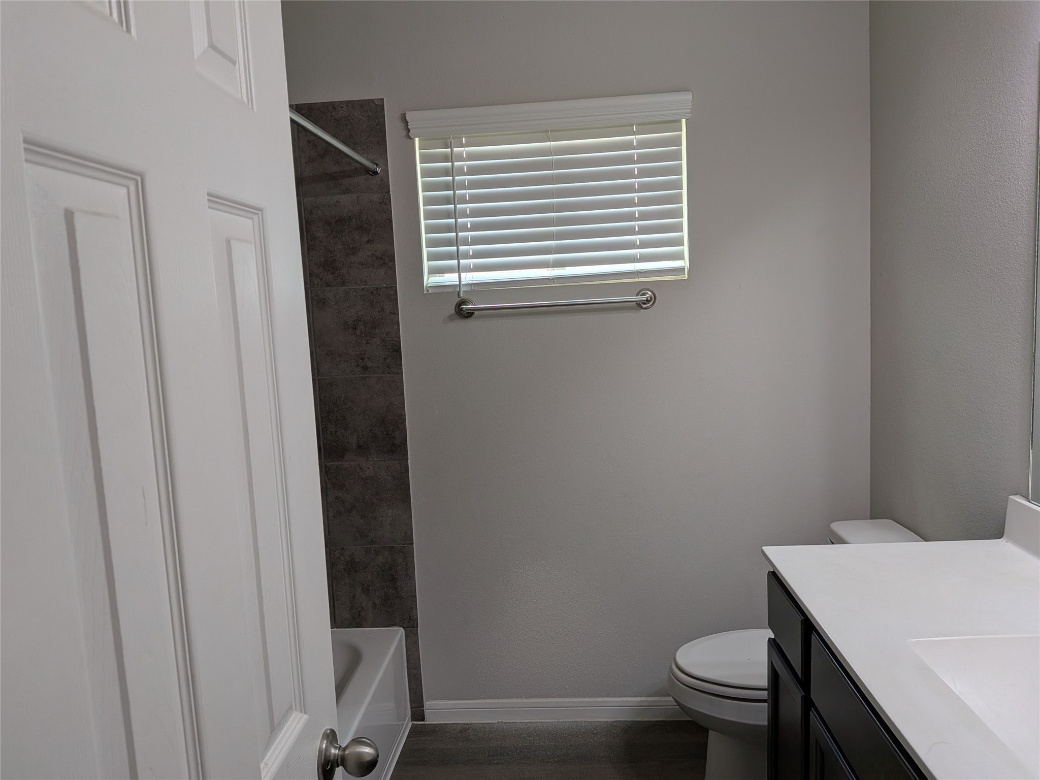 15730 Joe Dimaggio Street Splendora, TX 77372 - Photo 17 of 20 This photo shows a modern bathroom with a bathtub and shower, a window with blinds, a toilet, and a sleek vanity with a countertop. The walls and floor are in neutral tones, providing a clean and contemporary look.