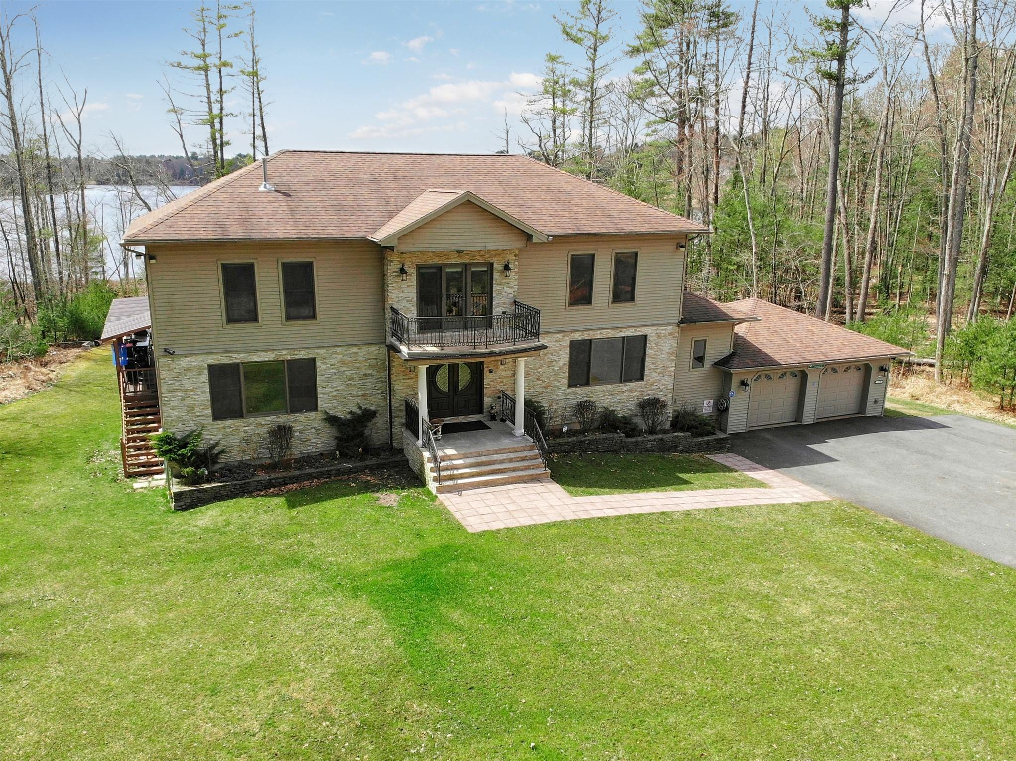 View of front of house with a front lawn, aphalt driveway, a balcony, a garage, and stone siding