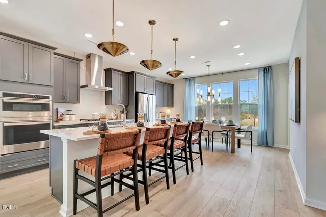 a kitchen with stainless steel appliances granite countertop a stove a refrigerator a kitchen island a dining table and chairs with wooden floor