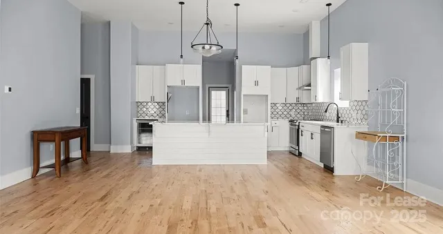 a large kitchen with stainless steel appliances kitchen island granite countertop a refrigerator a stove a sink dishwasher and white cabinets with wooden floor