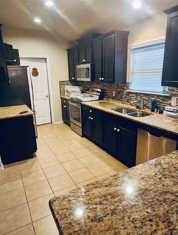 a kitchen with stainless steel appliances granite countertop a stove top oven a sink and a refrigerator