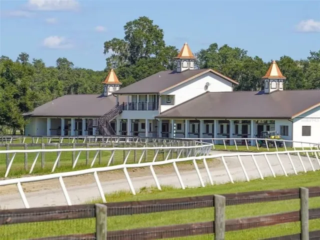 a white house with a large pool and lawn chairs under an umbrella