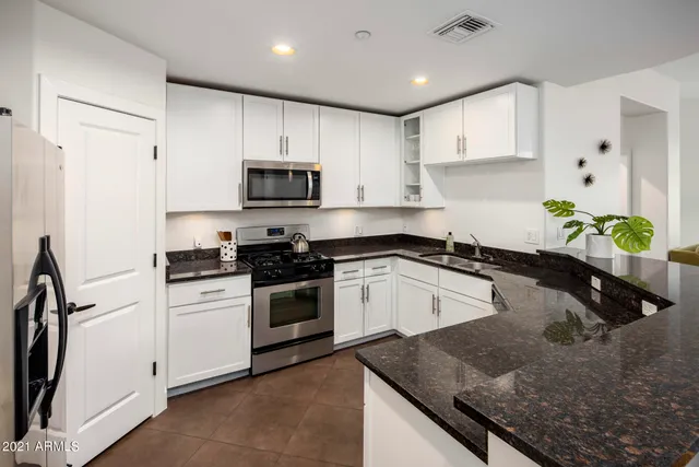 a kitchen with granite countertop a sink a stove top oven a refrigerator and white cabinets