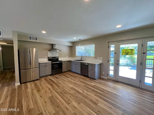 a kitchen with stainless steel appliances kitchen island granite countertop a refrigerator oven a sink with wooden cabinets and wooden floor