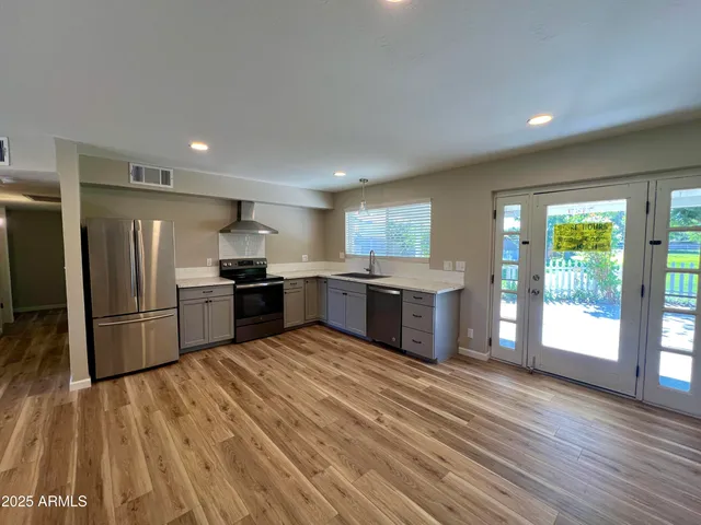 a kitchen with stainless steel appliances kitchen island granite countertop a refrigerator oven a sink with wooden cabinets and wooden floor