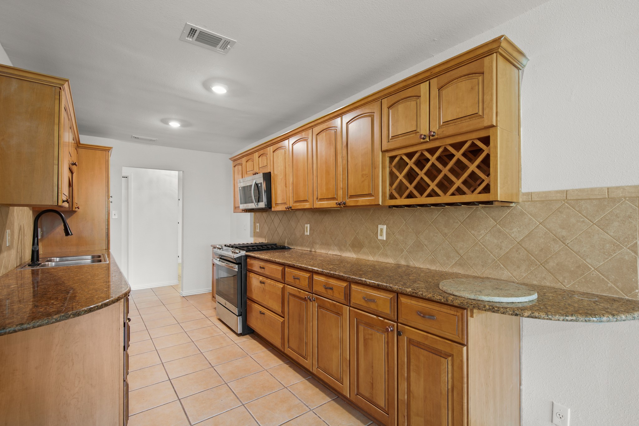 2109 Brandywine Lane Austin, TX 78727 - Photo 8 of 27 Kitchen featuring appliances with stainless steel finishes, backsplash, dark stone countertops, light tile patterned floors, and brown cabinets
