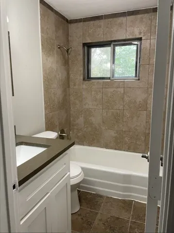 a bathroom with a granite countertop bathtub shower sink vanity and toilet