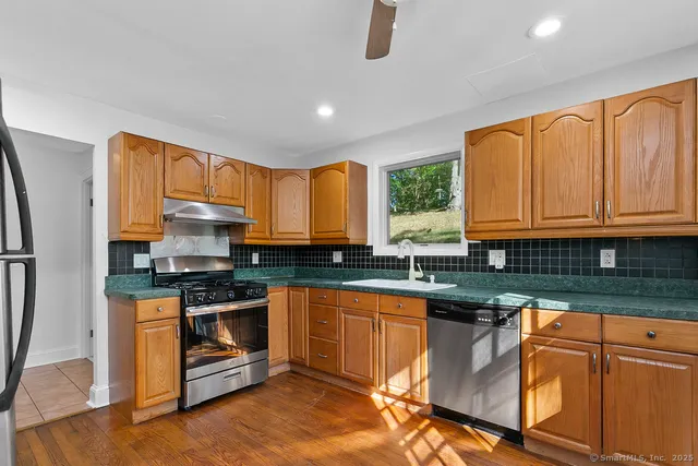 a kitchen with stainless steel appliances granite countertop wooden cabinets a sink dishwasher a stove and a refrigerator with wooden floor
