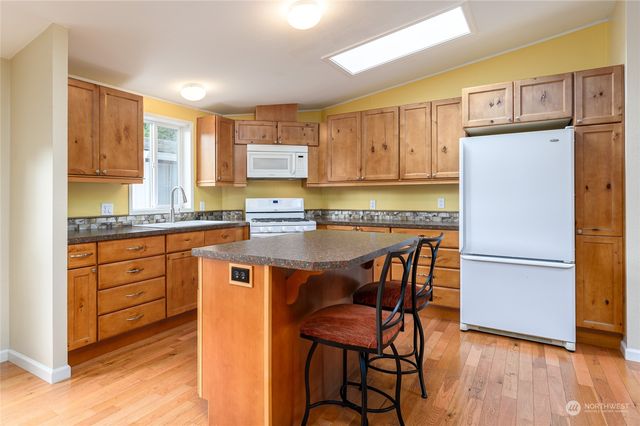 a kitchen with stainless steel appliances granite countertop wooden cabinets a refrigerator a sink a stove a dining table and chairs with wooden floor