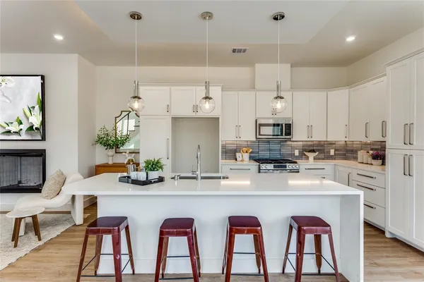 a kitchen with stainless steel appliances granite countertop a stove a sink a refrigerator and white cabinets with wooden floor