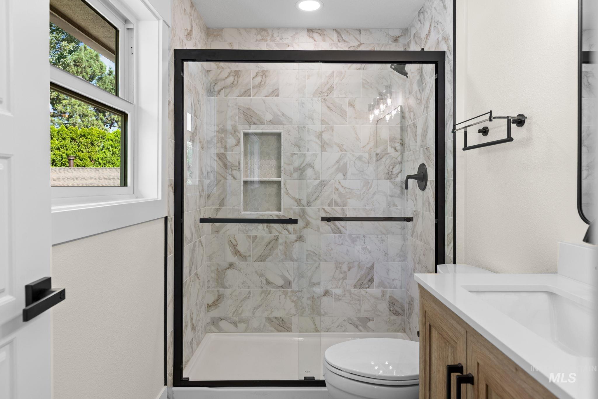 1675 Country Terrace Way Meridian, ID 83642 - Photo 19 of 50 Glass-enclosed shower with tiled walls and an integrated niche, a wood-finish vanity with a white countertop and undermount sink, and matte black fixtures throughout