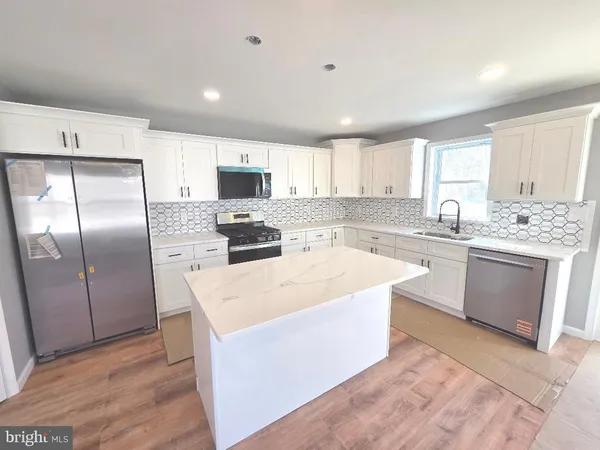 a kitchen with stainless steel appliances granite countertop a stove a sink a refrigerator and white cabinets