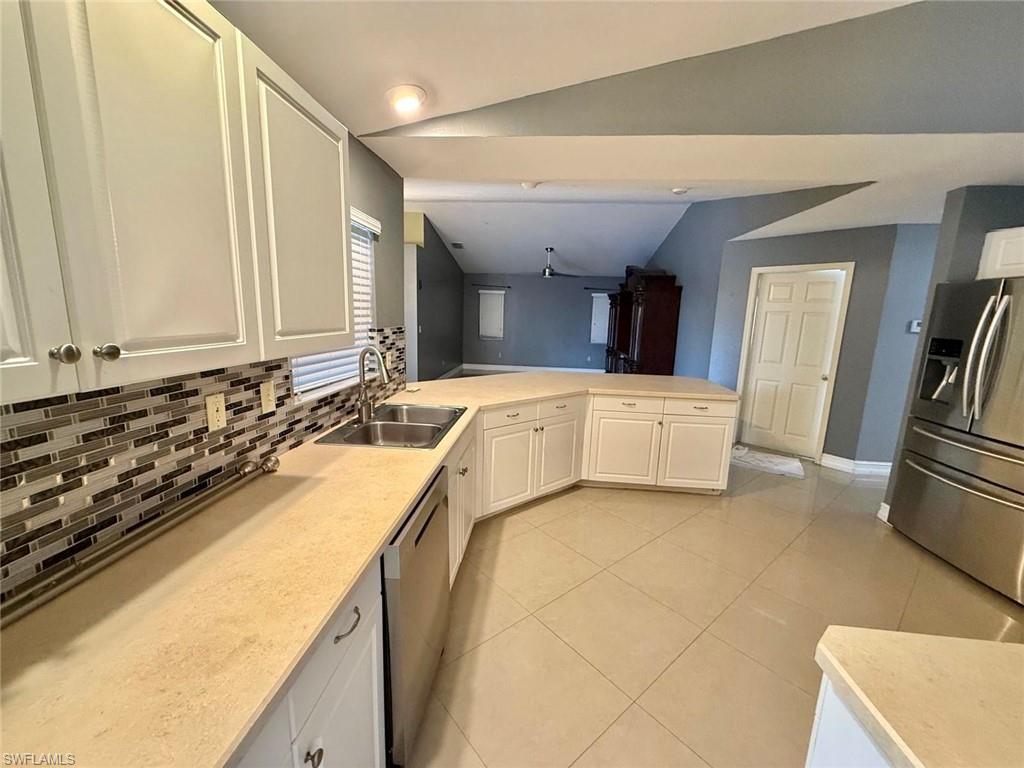 3908 Lee Boulevard Lehigh Acres, FL 33971 - Photo 5 of 24 Kitchen featuring vaulted ceiling, white cabinetry, sink, decorative backsplash, and stainless steel appliances
