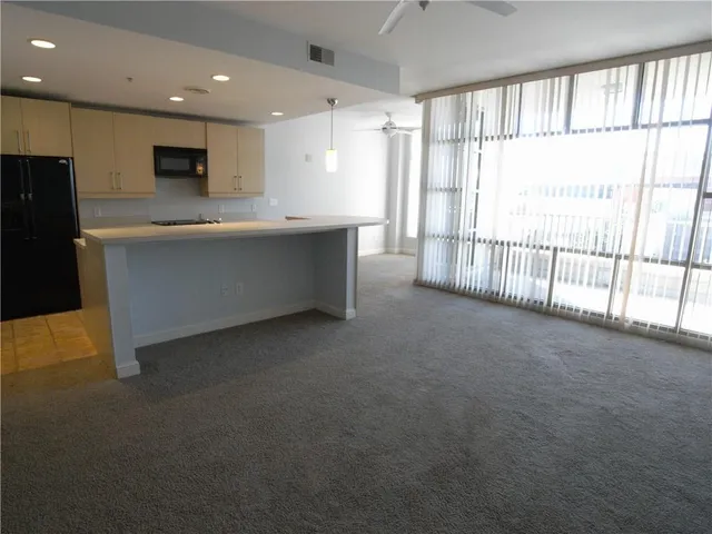 a view of an empty room with kitchen and window