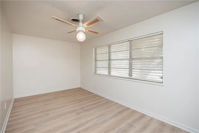 an empty room with wooden floor fan and windows