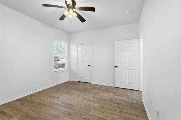 an empty room with wooden floor ceiling fan and windows