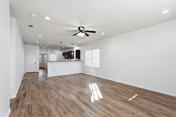 a view of empty room with wooden floor and kitchen view