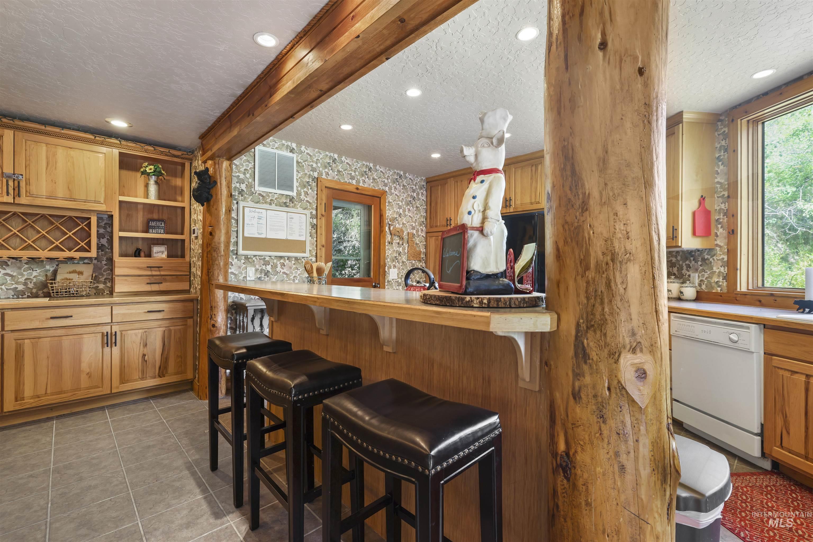 224 Dakota Road Mountain Home, ID 83647 - Photo 12 of 50 Rustic kitchen bar featuring a wood-finish countertop, prominent wood beam supports, recessed lighting, tile flooring, and integrated wood cabinetry with a wine rack